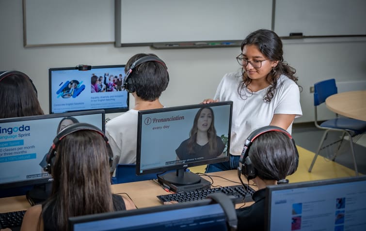 Una niña enseñando inglés a otra en una sala de computación.